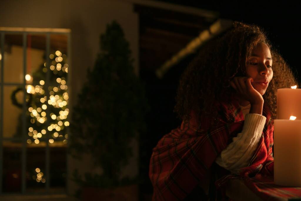 A woman wrapped in a plaid blanket sitting beside glowing candles at night, enjoying a peaceful moment during the cozy season of love.